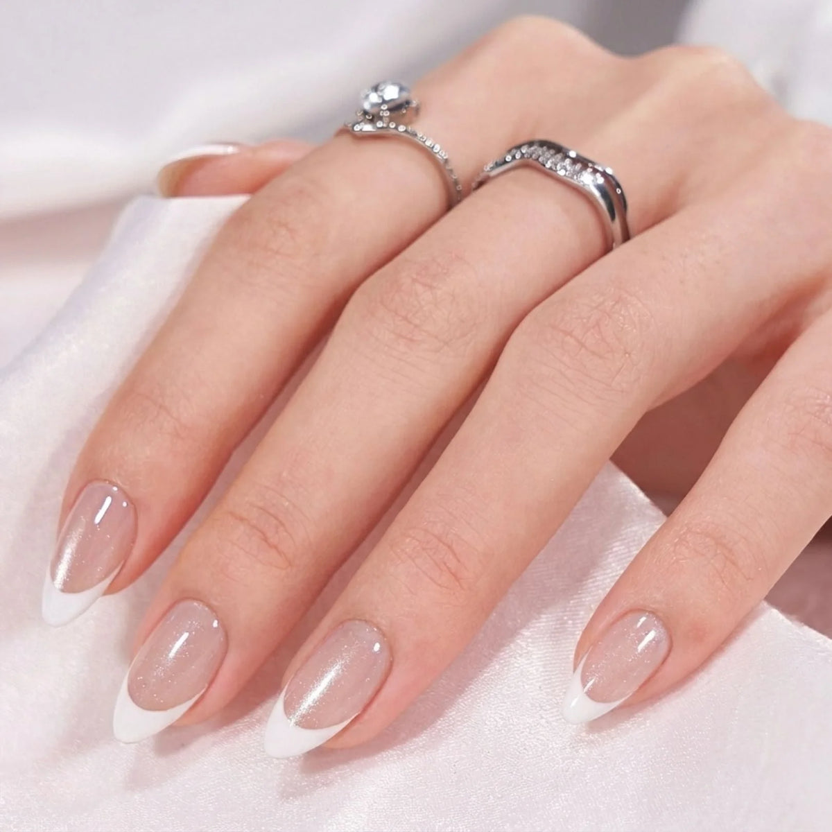 Faux ongles Sweet Sprinkle en gros plan – forme amande, bout french blanc, bagues argentées sur satin blanc
