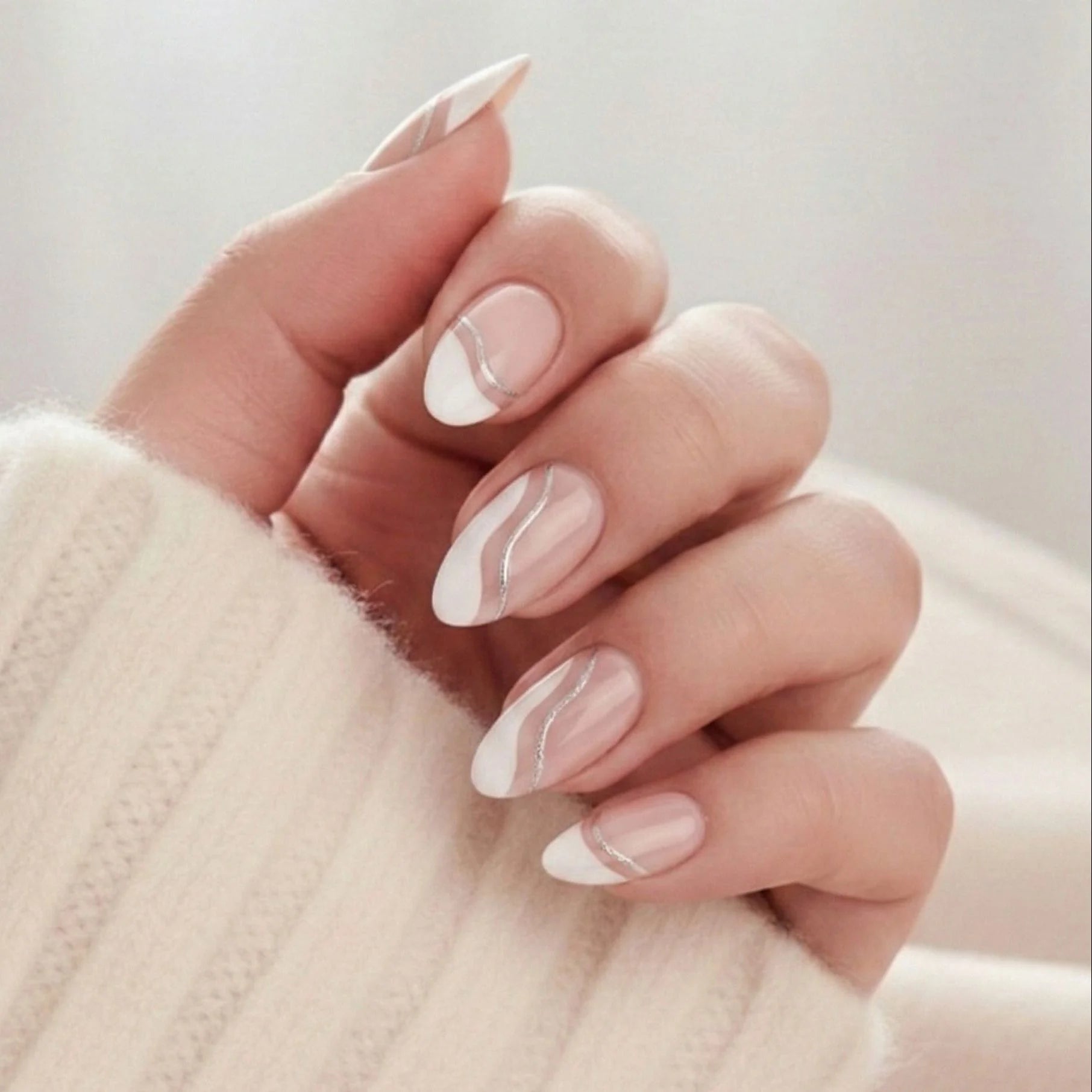Metallic Merge press-on naglar – mandelformade lösnaglar med vit fransk tipp och silvrig swirl mot beige tröja