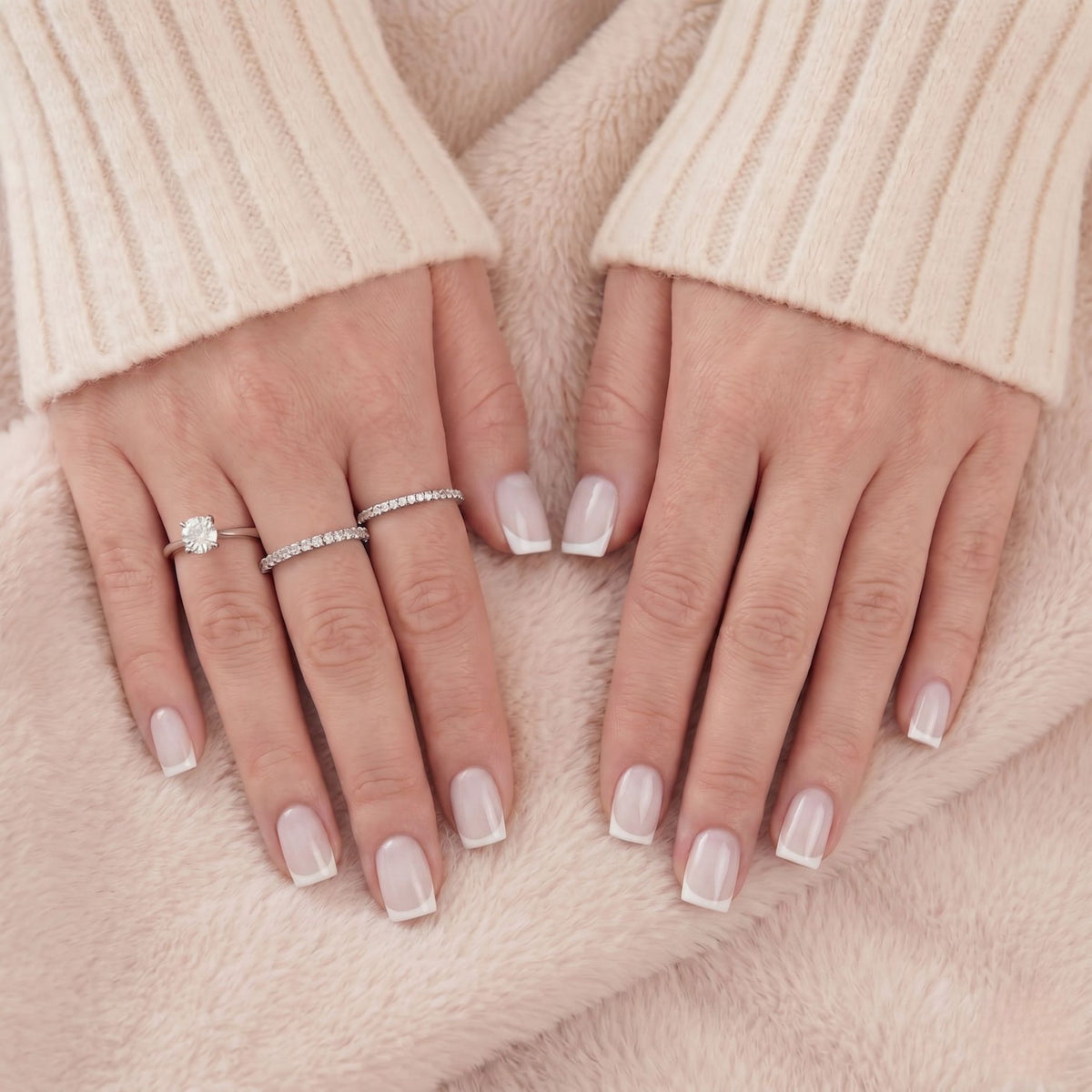 Gros plan de faux ongles french blancs courts square et bagues en argent sur fourrure beige