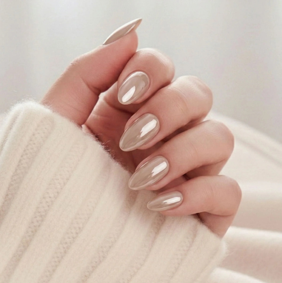 Faux ongles Pearly Perfection, forme amande en pearl taupe avec éclat métallique sur un pull tricoté blanc crème