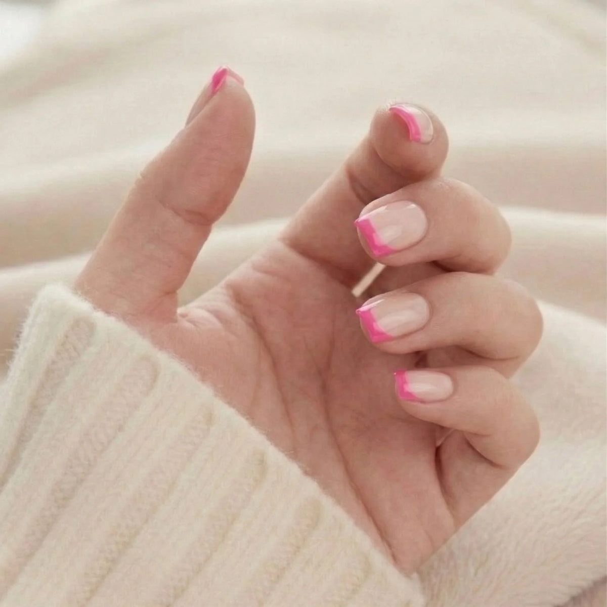 Faux ongles carrés courts Pixie Pink, pointe française rose vue vers le haut sur un pull tricoté