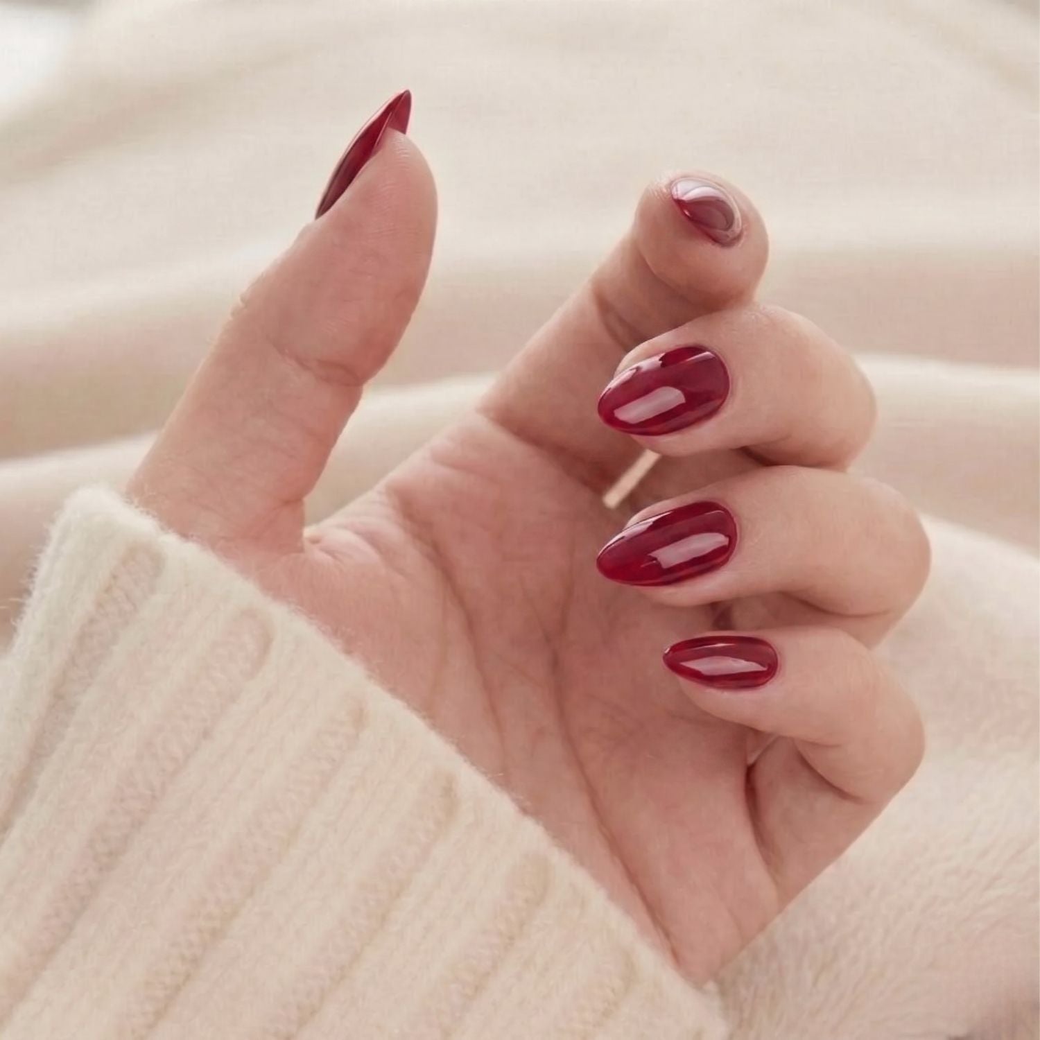Ruby Romance: Glansiga vinröda mandelformade press-on naglar, en elegant lösnagelsmanikyr på hand i mjuk tröja
