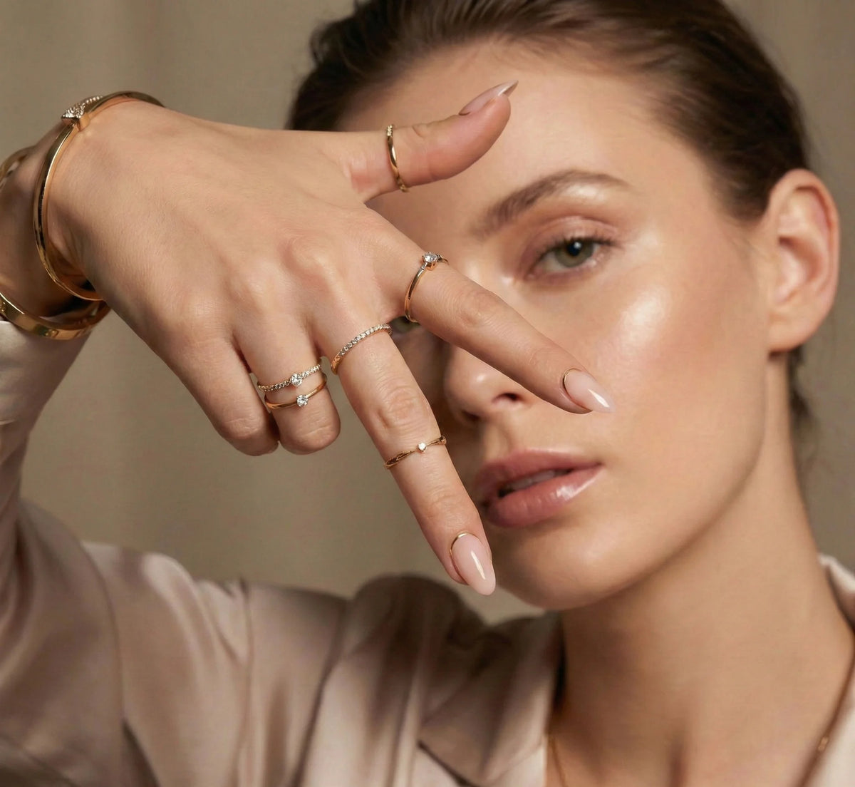 Modèle élégant présentant des ongles amande nude press-on à liseré doré, avec des bagues en or.