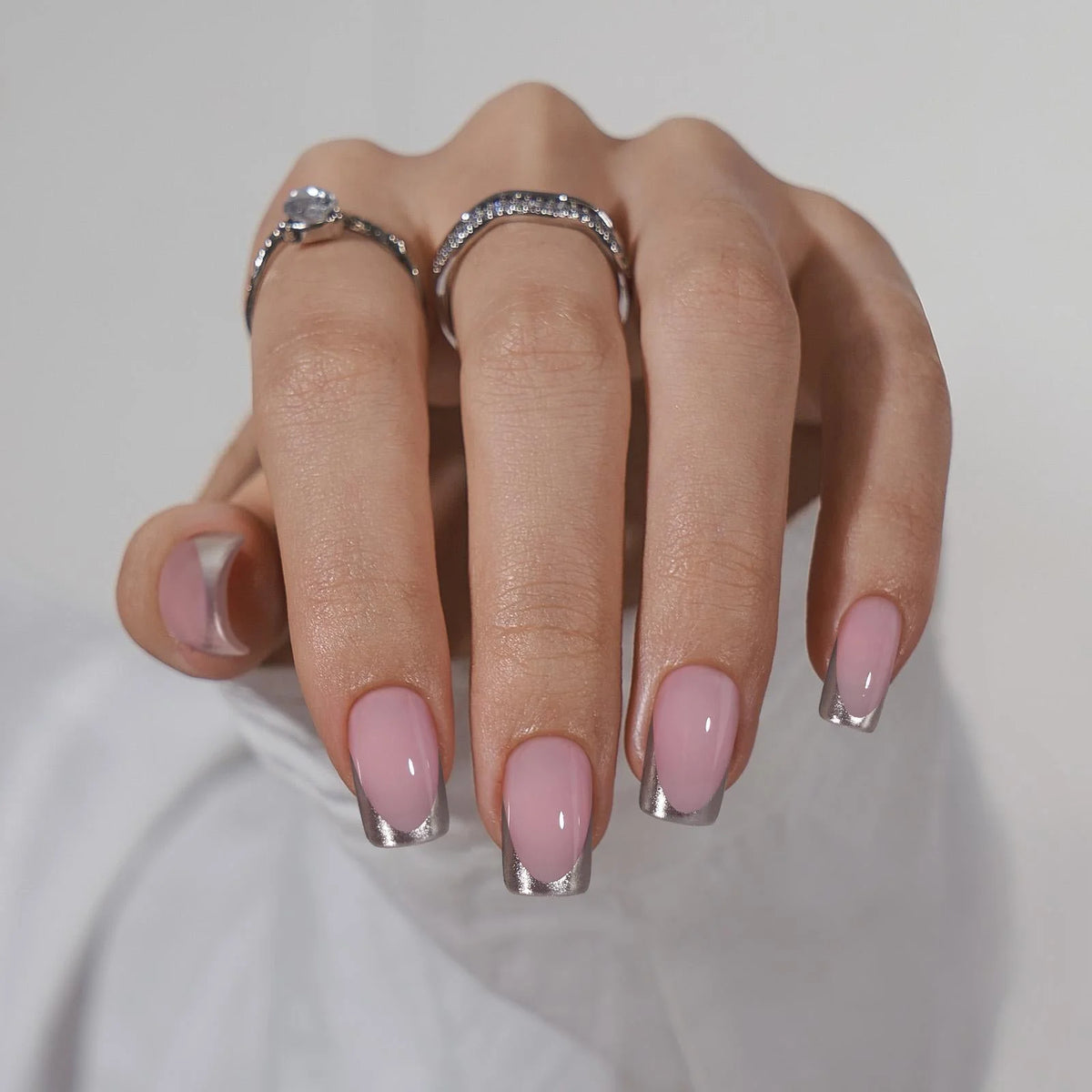 Faux ongles Fancy French en situation, ongles carrés nude avec pointe argentée et bagues en cristal