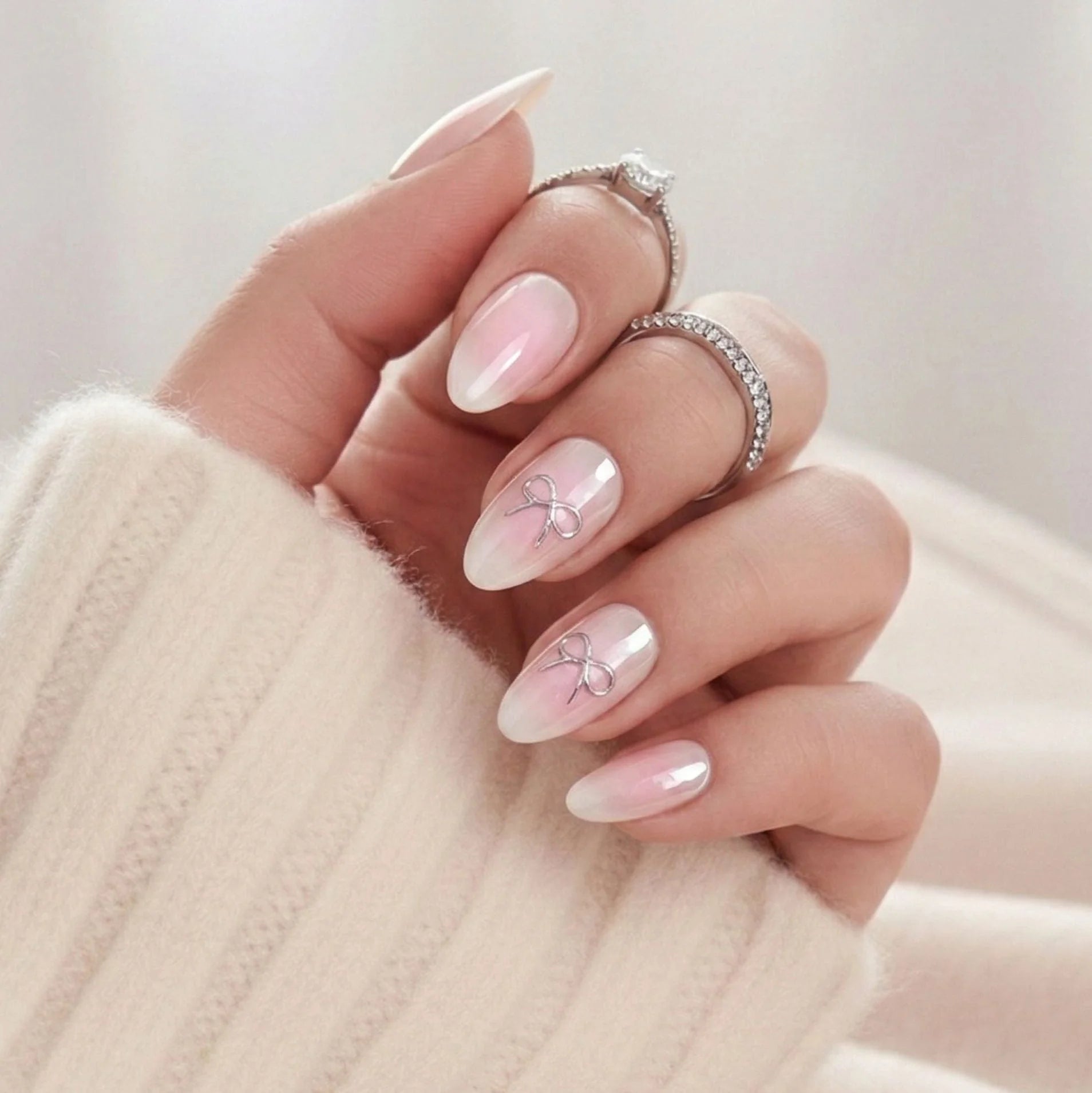 Aura Amoré press-on naglar – rosa aura med silverrosett accent i mandelform mot creme stickad tröja