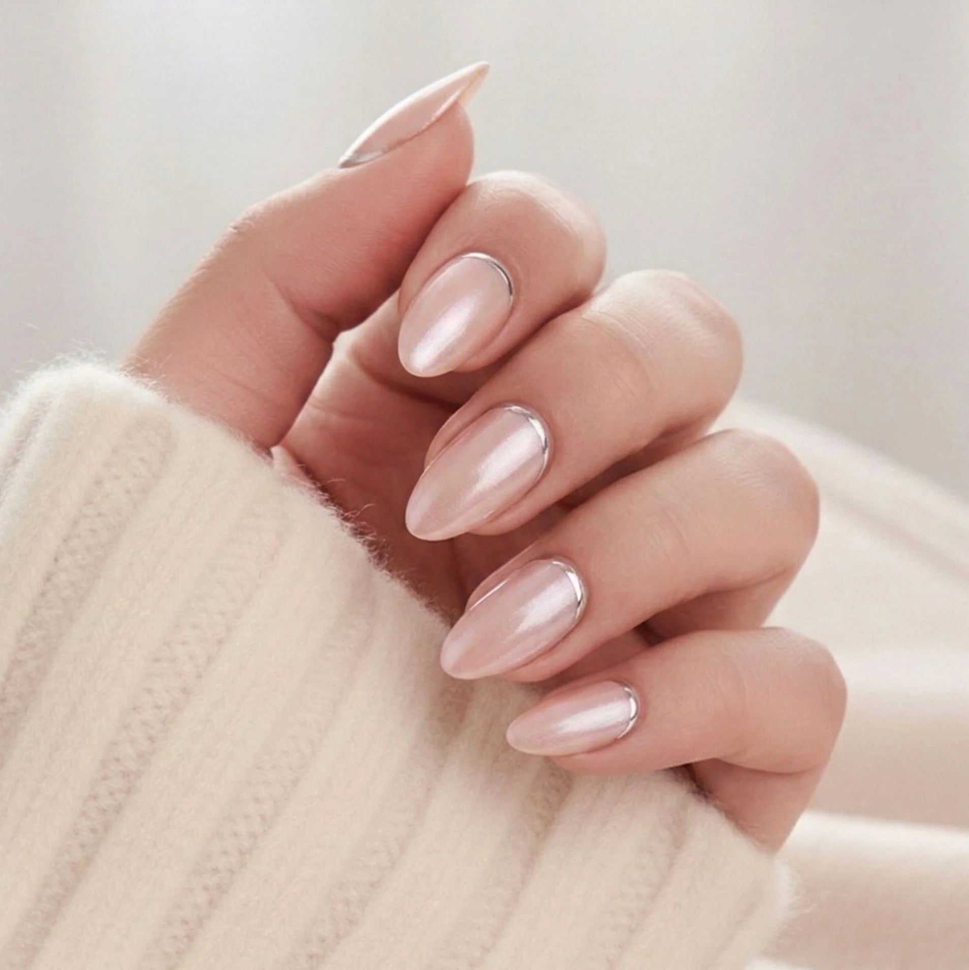 Shimmering Silver press-on naglar – mandelform i pearl nude med silverkant vid nagelbandet mot vit stickad tröja