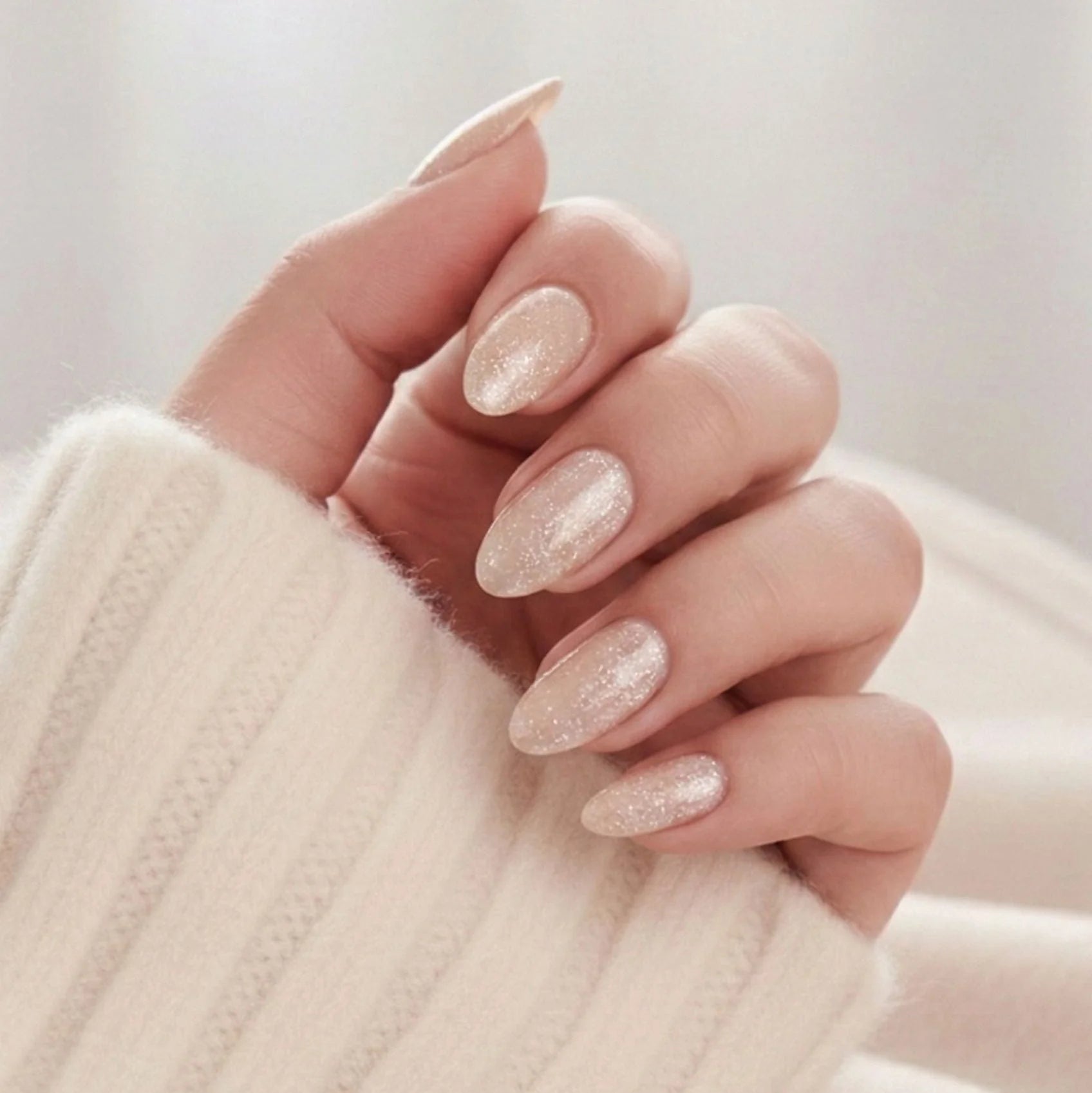 Candy Chrome press-on naglar – champagne glitter shimmer i mandelform mot creme stickad tröja