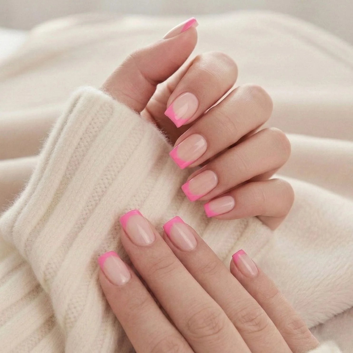 Pixie Pink naglar på hand – rosa french tipp korta square mot beige stickad tröja