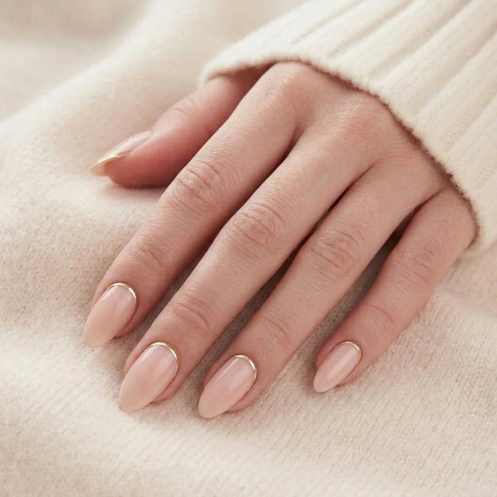 Golden Glimmer naglar på hand – peach nude mandel med guld-detalj mot beige stickad tröja