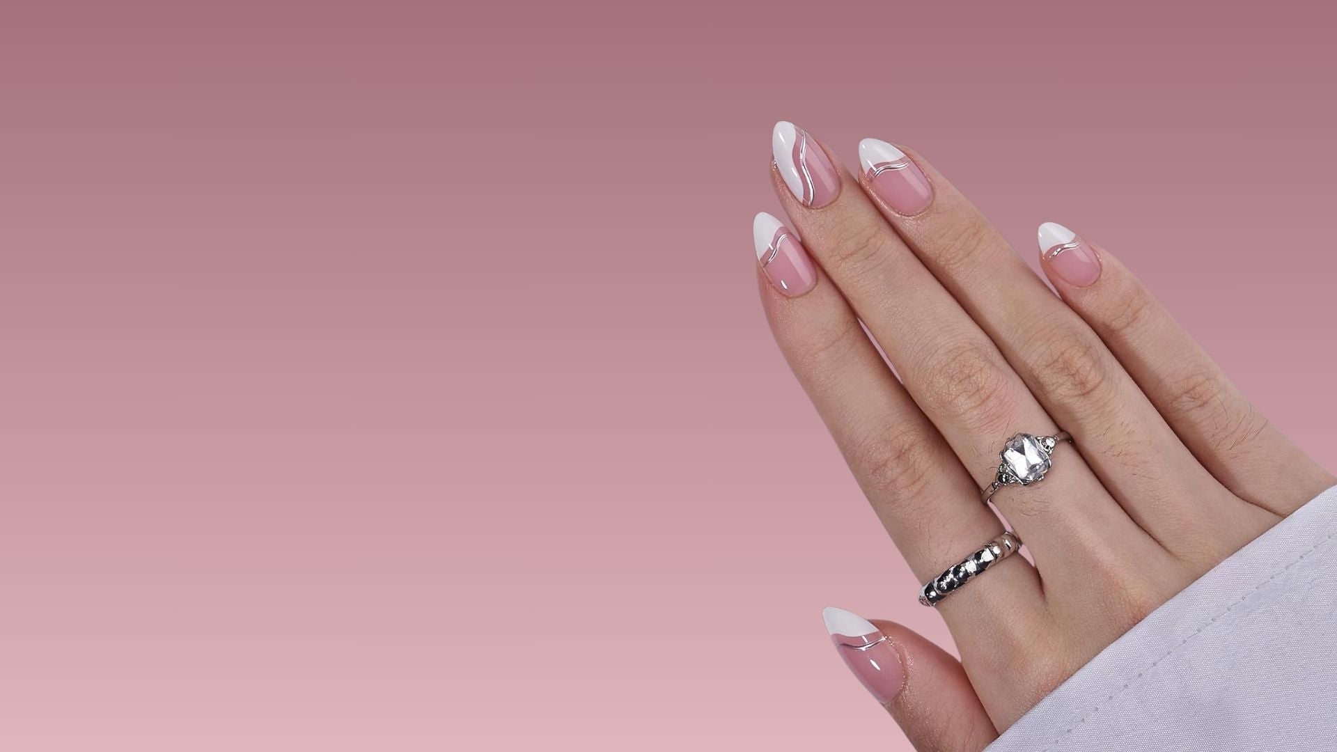 Mandelformade press-on naglar i rosa och vitt med modern fransk design och eleganta silverdetaljer på en hand