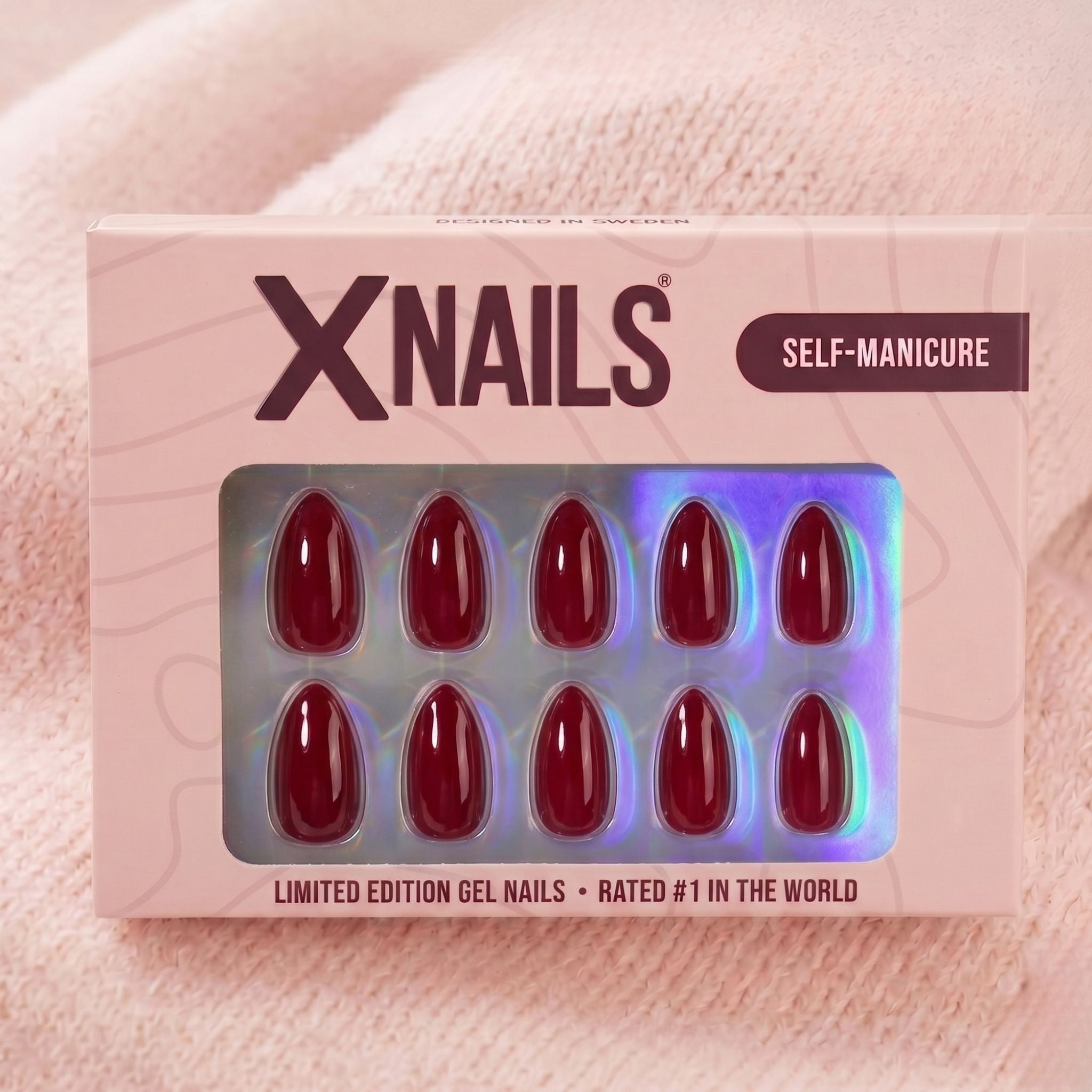 XNails-förpackning med vinröda almond press-on naglar mot rosa stickad bakgrund