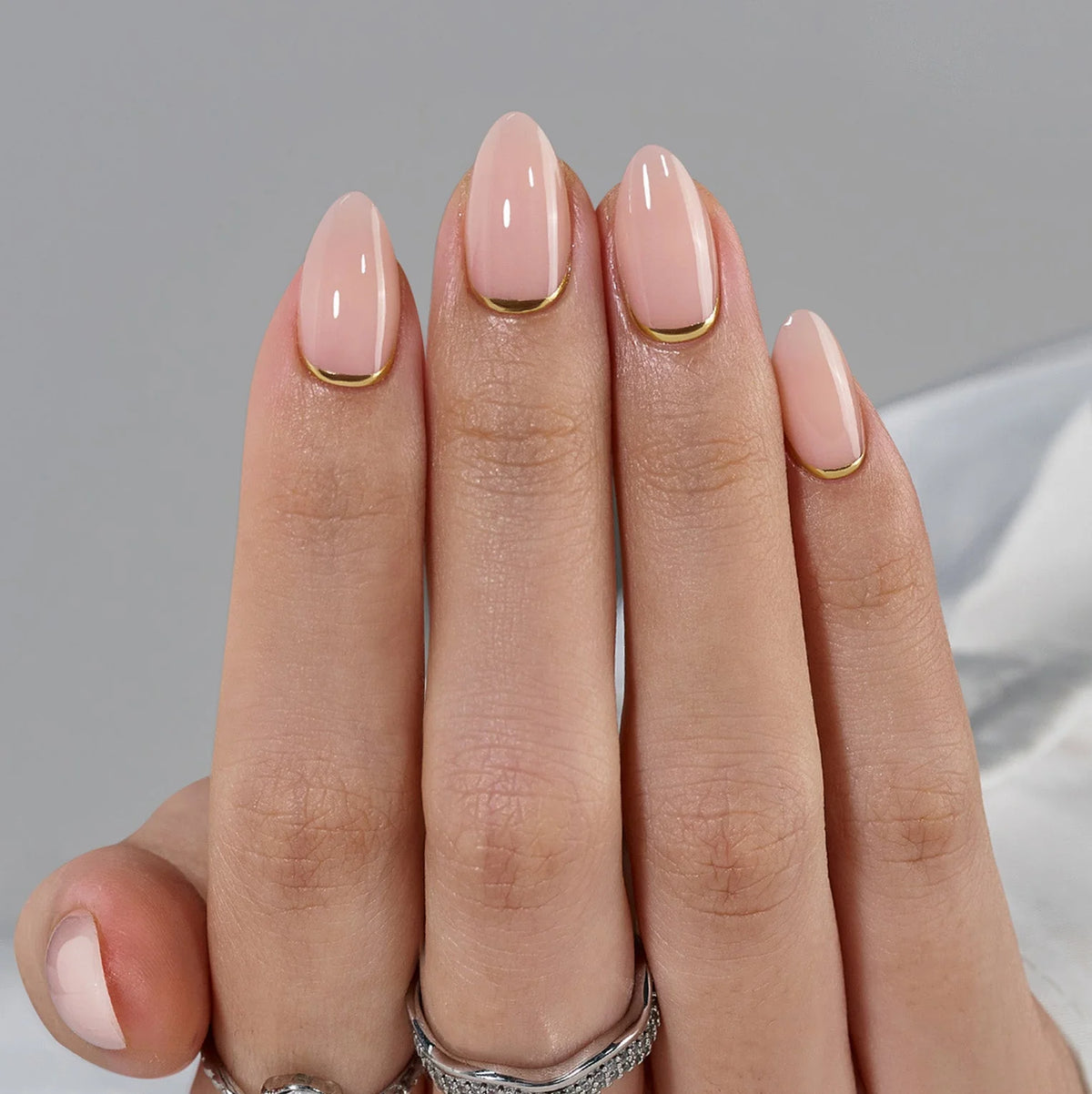 Gros plan sur les faux ongles Golden Glimmer, base nude et ligne dorée le long de la cuticule