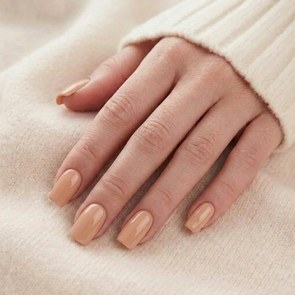 Honey Heaven faux ongles dans un ton nude/miel uni sur une main, devant un pull tricoté beige