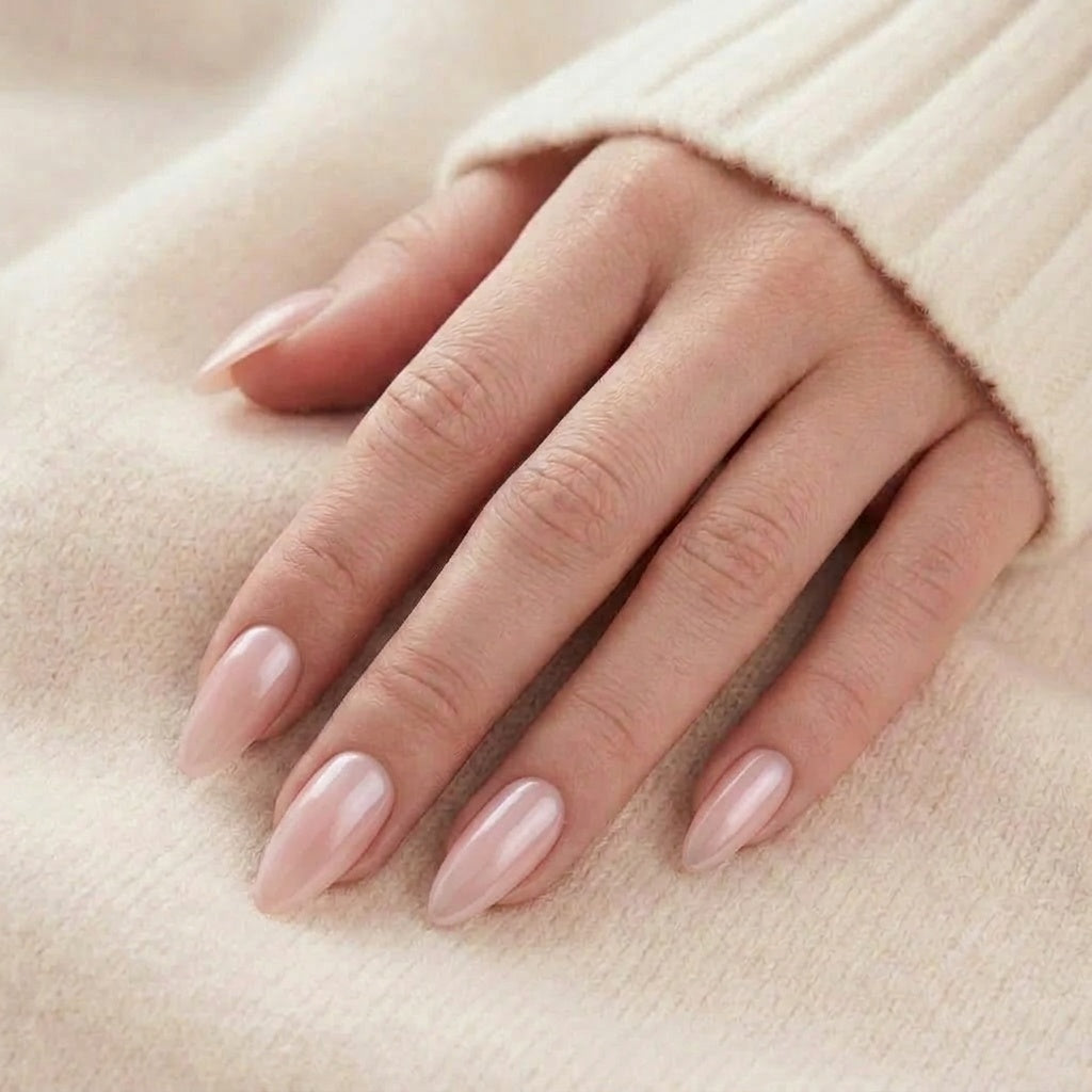 Pinkie Pearl faux ongles en rose nude laiteux brillant avec éclat nacré sur faux ongles amande longs, devant un pull tricoté beige