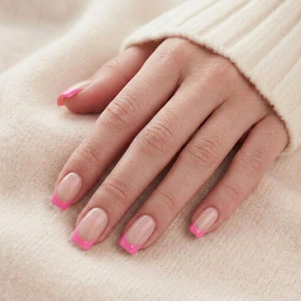 Pixie Pink faux ongles carrés courts avec base nude et French tip rose vif sur une main, devant un pull tricoté beige